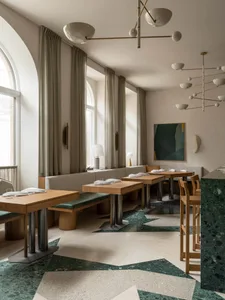 Modern restaurant interior with concrete walls, multiple tables, benches, and hanging lamps creating a warm atmosphere