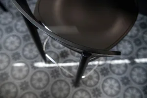 A modern indoor space with a black metal chair on a wooden base, set against a backdrop of white and grey tile flooring