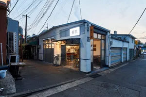 A well-lit Asian restaurant with a white exterior, glass door, and wooden furniture, creating a comfortable dining atmosphere