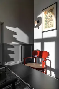 A dimly lit room with a red chair near a window, creating a cozy atmosphere with two chairs and a comfortable ambiance