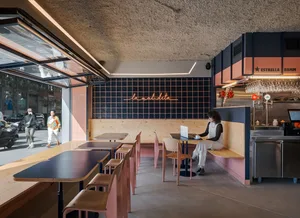 A modern cafe interior with a woman working at a table, surrounded by wooden and brick walls, comfortable seating, and natural light