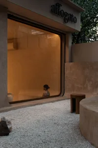 A woman stands in front of a window in a calm and serene room with a stone wall, a bench, and two bowls on surfaces