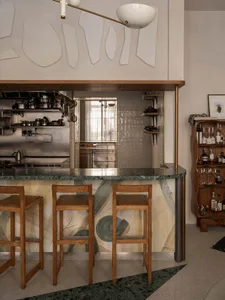 A kitchen with a marble countertop, wooden stools, and three chairs, conveying a warm and inviting atmosphere for gatherings and socializing