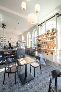 A cozy cafe with wooden tables and chairs, a kitchen in the background, and various items on the tables