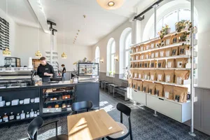 Cozy coffee shop with a large wooden dining table, comfortable seating, and decorative items such as cups, bottles, and potted plants
