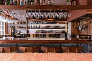 A cozy bar area with a wooden countertop, wine bottles, and comfortable seating for patrons