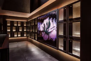 A gallery space featuring a large floral painting on a wall, with a vibrant pink flower design against a neutral background