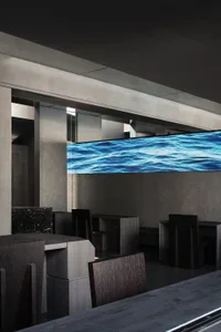 Modern restaurant interior with a large screen TV above a dining table, surrounded by chairs and a comfortable seating area