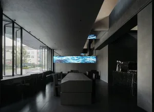 Dark and moody restaurant with black walls, a large screen, and scattered chairs
