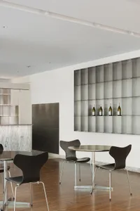 Modern restaurant dining area with tables, chairs, and silver walls, featuring wine bottles and warm lighting