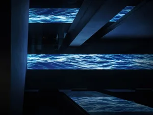 Modern living space with a large blue water-like design on the wall, two tables, and a chair, creating an underwater ambiance
