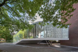 A modern building with a curved roof and several windows, surrounded by trees in an urban environment