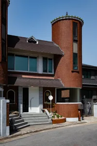 A residential house with red brick walls, featuring two towers and a large window, set in a traditional and modern residential area