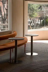 Two orange couches in a well-lit living space with large windows, round tables, and a comfortable atmosphere