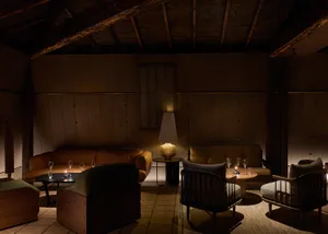 A warm and inviting dining space with a wooden floor and walls, featuring a dining table, chairs, and couches, with wine glasses on the table