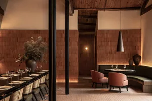 Sophisticated dining area with a long wooden table, chairs, and a smaller table, set with wine glasses, in a warm and inviting atmosphere