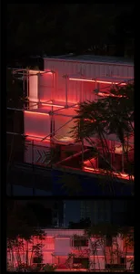 A modern building at night with red lights illuminating its exterior, featuring multiple levels and a balcony, with two chairs in front for outdoor seating or event setup