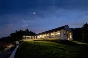 一棟白色房屋，窗內燈光亮起，背景是雲層密布的夜空，可見皎潔月光