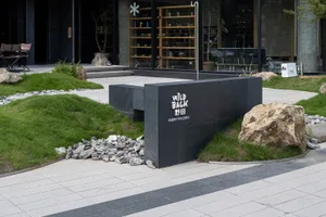 A serene outdoor space with a black stone bench and potted plants surrounding a building