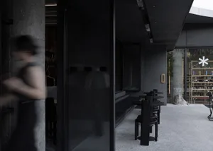 A dark restaurant interior with a black doorway, chairs, and a mysterious atmosphere