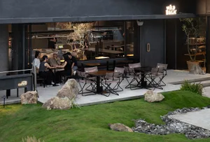 An outdoor dining area with several tables and chairs, surrounded by potted plants, creating a comfortable and inviting atmosphere for socializing and enjoying meals in an open-air setting