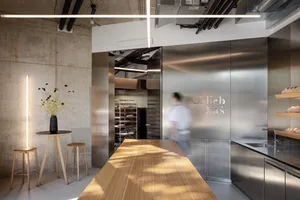 A modern kitchen with a wooden table and two ovens, surrounded by chairs, in a well-lit space with a focus on functionality and aesthetics
