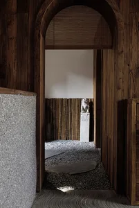 Wooden hallway with statues and a bench, featuring a doorway to another room