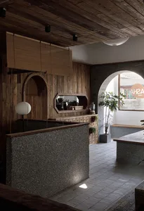 Warm and inviting restaurant interior with wooden walls and floors, featuring two dining tables, potted plants, and comfortable seating options