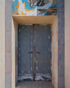 A traditional doorway with a metal frame and stone arch, set in a historic building with a wooden door and rustic appearance