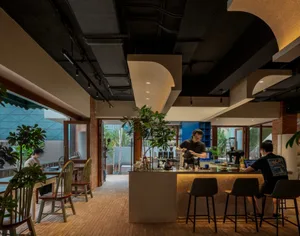 Warm and inviting restaurant interior with a bar area, dining tables, and potted plants, featuring brick walls and a rustic atmosphere