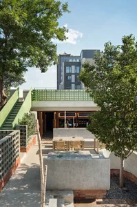 A modern outdoor space with a patio, dining table, and chairs, surrounded by potted plants and a green wall, with a warm and inviting atmosphere
