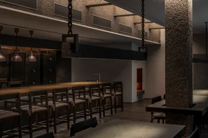 Dimly lit bar area with a wooden counter, stools, and chairs, creating a cozy ambiance