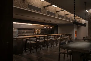 Dark and empty restaurant with a long bar counter and chairs, dimly lit with bottles on the counter