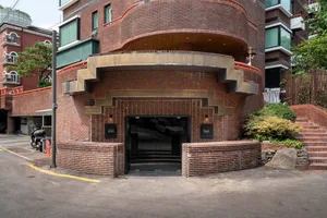 一座建築物的渲染場景，擁有大型磚牆立面、拱門與樓梯，前景有兩輛車與三人