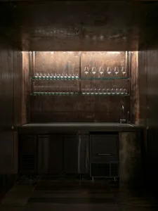 A dark kitchen with a black refrigerator freezer and wine glasses placed throughout, creating a cozy and inviting atmosphere