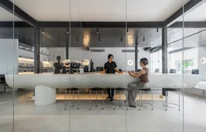 Modern interior design showroom with a white marble bar, black chairs, and a dining table, featuring two women in a social setting