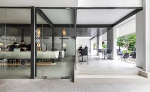 A modern cafe interior with a glass door, chairs, a dining table, and clocks, set in a spacious area with ample seating options
