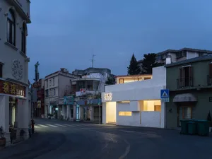 夜間街景，白色店面與周圍城市景觀，搭配盆栽與長椅