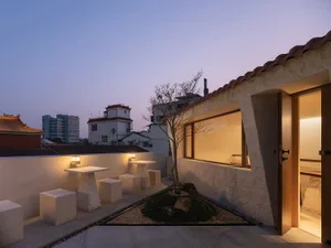 An inviting outdoor patio with a white building in the background, featuring tables and chairs, and string lights for nighttime ambiance