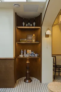 A wooden shelf in a kitchen or dining area holds various items such as bottles, cups, bowls, and books, adding warmth and character to the space