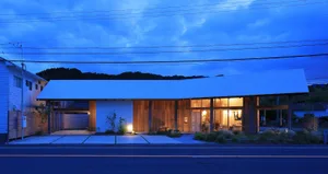 A well-lit white house with a wooden structure at night, surrounded by potted plants and two benches, conveying a sense of comfort and relaxation