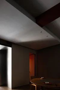 A dimly lit hallway with a gray wall and a doorway leading to another room