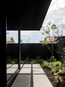 A modern outdoor patio with a black wall, glass door, potted plants, and a TV mounted on the wall, creating a lively and inviting atmosphere