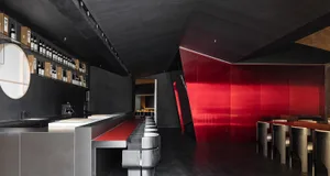 Modern restaurant interior with a long counter, red accents, and books scattered throughout, exuding a stylish and contemporary vibe