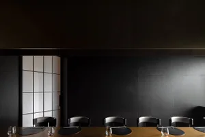 A modern dining area with a long black table and multiple chairs, set for a formal dinner with wine glasses, cups, and utensils