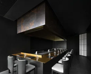 Modern commercial kitchen with a large black countertop, dining table, and chairs, featuring various utensils and a hood for cooking