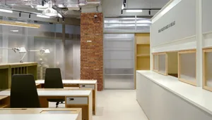Modern workspace with a brick wall, wooden furniture, and bookshelves, featuring a mix of seating and study areas