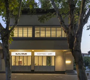 一座現代建築擁有兩間店面，包括咖啡店與藝術畫廊，特色為大片窗戶、盆栽、椅子與餐桌