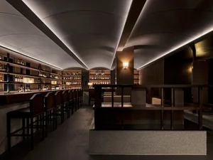 A cozy bar area with wooden furniture, dining tables, and a bar counter displaying bottles, set in a warm and inviting atmosphere