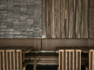 A modern dining space with wooden walls, three dining tables, and benches, creating a warm and inviting atmosphere